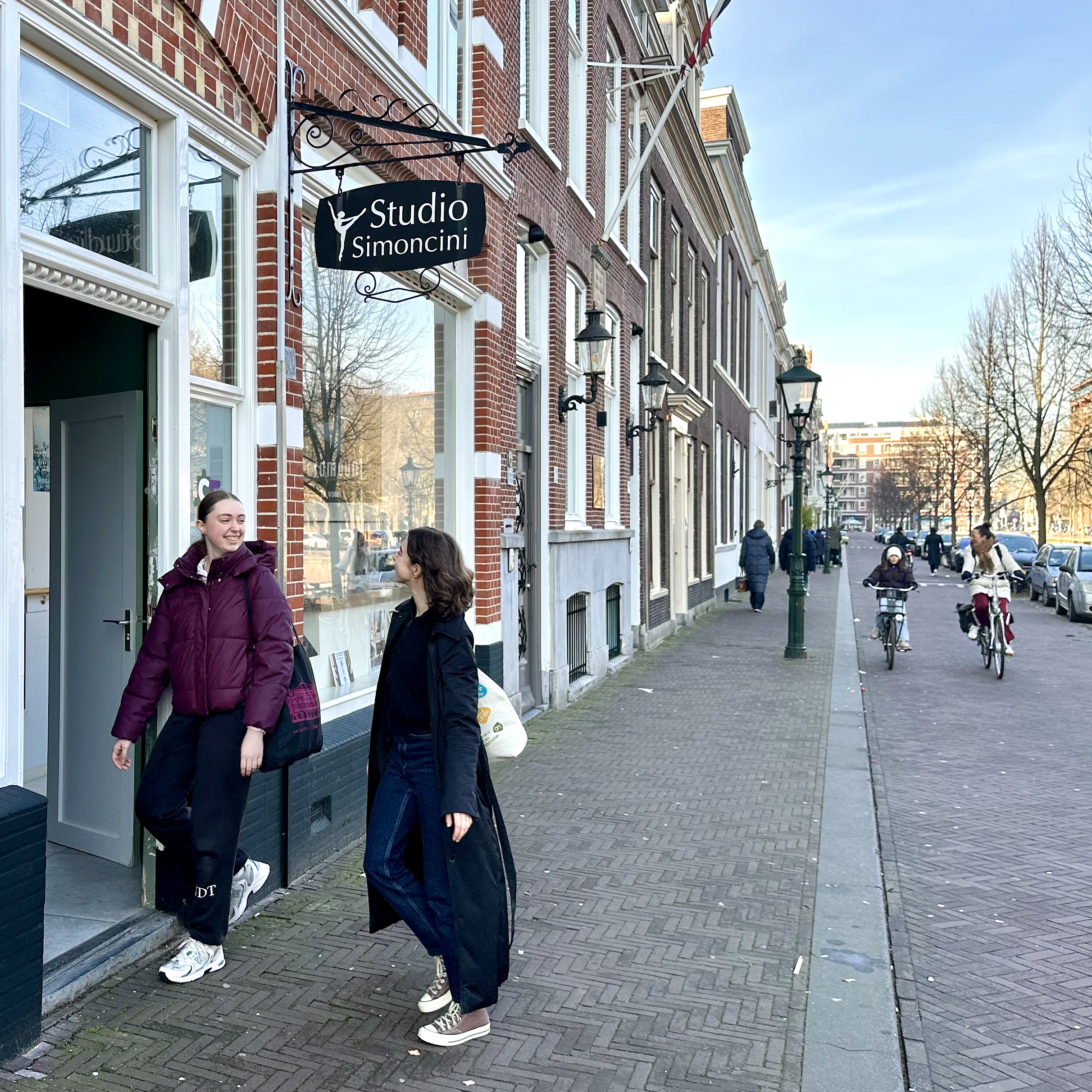 Twee volwassen vriendinnen stappen de voordeur binnen bij Studio Simoncini. Een van hen is student bij de balletschool, de ander is vriendin die mee komt doen.